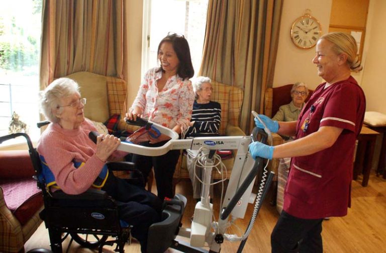The manager and a care assistant help lift a lady out of her chair
