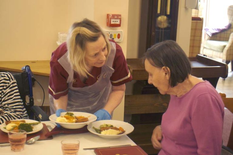 One of the staff offers a choice of lunch to a resident